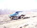 1996 Ford Bronco - A green Ford Bronco navigates a challenging muddy terrain, kicking up dirt as it goes.