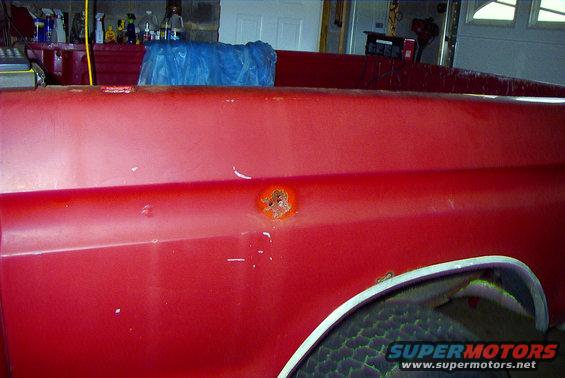 Red pickup truck bed with rust spot and dent. Visible tire and chrome trim