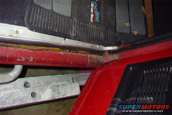 Close-up of a red truck's interior door sill with floor mats and rust