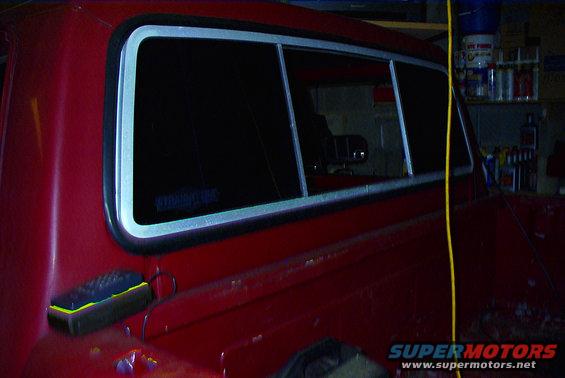 Side view of a red pickup truck's rear window and fuel door