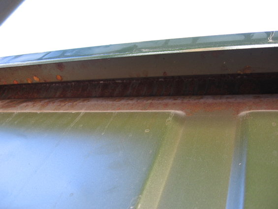 Close-up of a rusted metal seam on a green painted surface