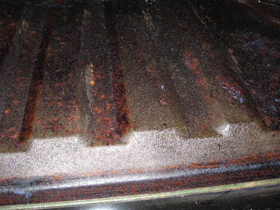 corroded metal bed floor with ribbed texture, some white residue visible