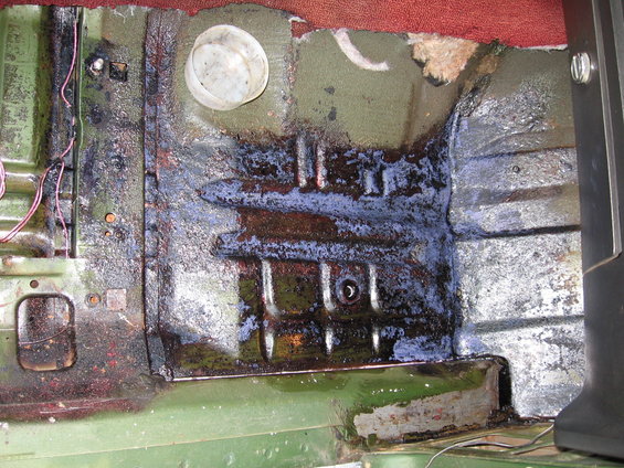 Vehicle floor with rust, blue and brown stains, and exposed wiring