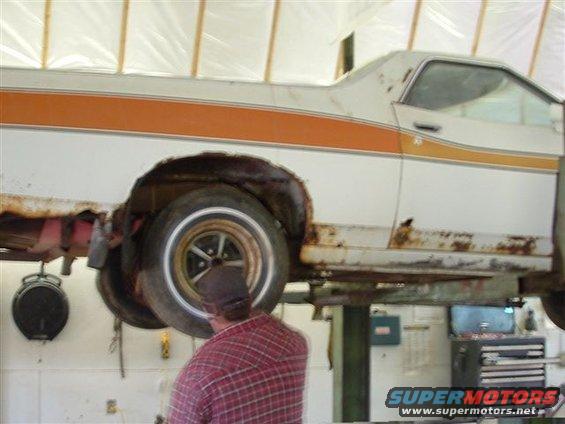 1975 Ford Ranchero on a lift, showing rust around the rear wheel well and lower body panels