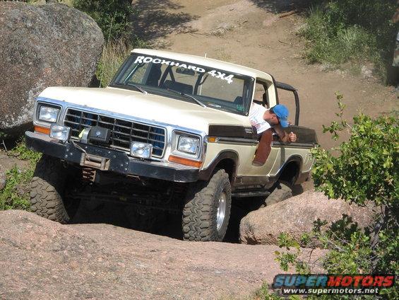1979 Ford Bronco 3q-front view, off-roading over rocks. White and brown