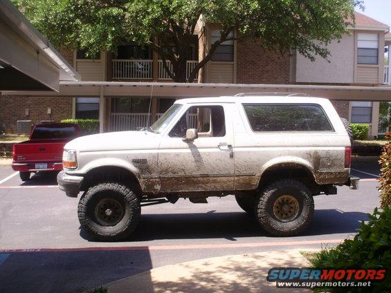 White Ford Bronco parked next to a red pickup truck. It's covered in mud
