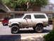 1992 Ford Bronco - A muddy white 1992 Ford Bronco is parked in a lot next to a red pickup truck.