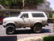 1992 Ford Bronco - A muddy white 1992 Ford Bronco is parked outside an apartment building.