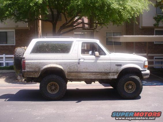 White 1992 Ford Bronco parked on pavement, covered in mud. It has a spare tire mounted on the back