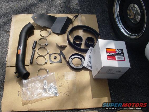 K&N air intake kit laid out on cardboard, including a black intake tube, heat shield, clamps, and a filter box