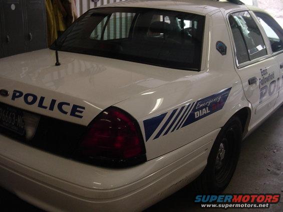 2002 Ford Crown Victoria police car, rear quarter view. Blue 'POLICE' text on trunk lid and 'Emergency DIAL' graphic on rear fender