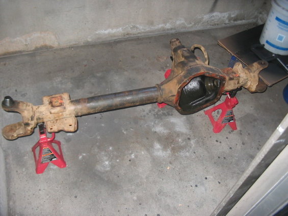 Front axle assembly on jack stands. It's rusty and has oil in the differential housing