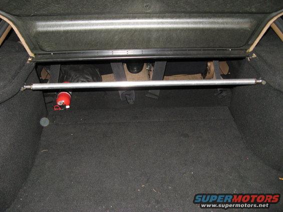 Car trunk interior with a silver strut bar across the top and a red fire extinguisher mounted on the left