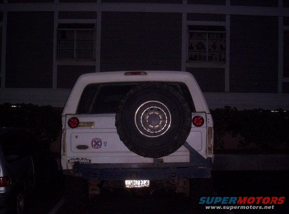 Rear view of a white Ford Bronco with a spare tire mounted on the back. It has a blue bumper and a license plate