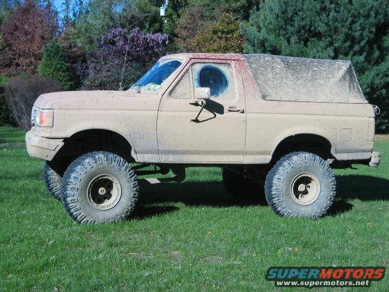 Mud-covered 1990 Ford Bronco with a soft top and lifted suspension, parked on grass