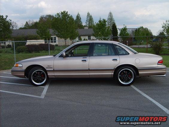 Side view of a tan Ford Crown Victoria with black rims and red brake calipers parked in a lot