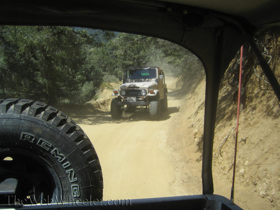 Toyota Land Cruiser FJ40 in front of another off-road vehicle on a dusty dirt road