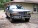 1996 Ford Bronco - This Ford Bronco is parked in front of a weathered house with trees in the background.