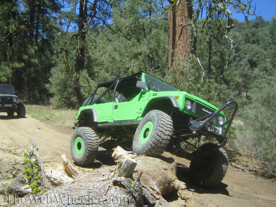 green off-road vehicle with big tires on a dirt trail, another jeep in background