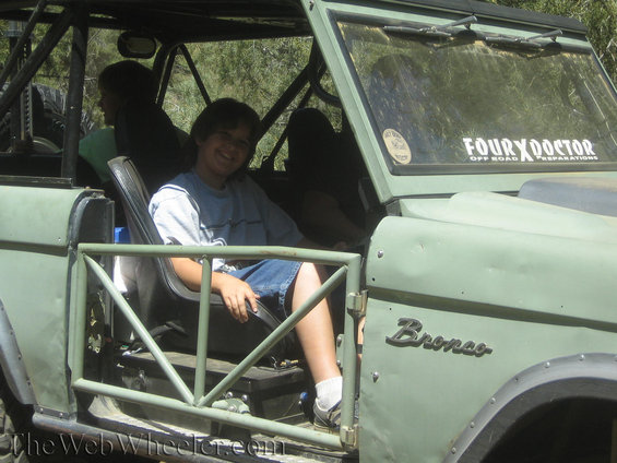 Green Ford Bronco interior with a young person smiling in the driver's seat; roll cage visible