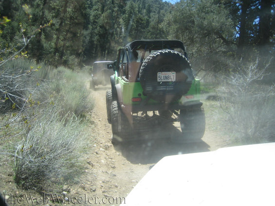 Green off-road vehicle with spare tire on back, driving on a dirt road