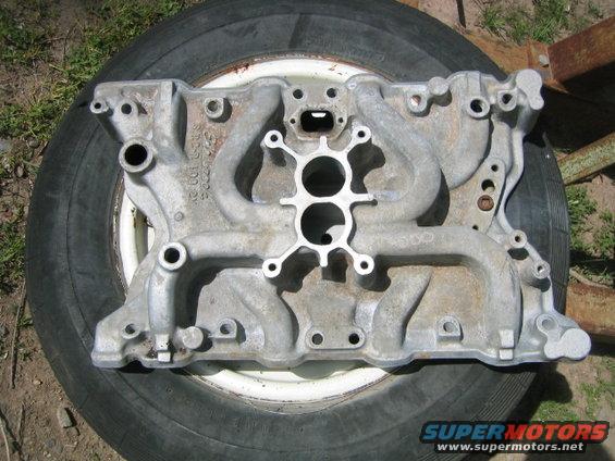 Aluminum intake manifold with dual carburetor openings, resting on a tire