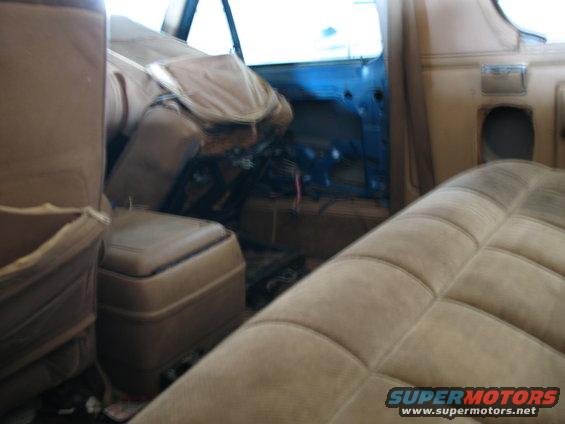 Interior view of a vehicle with seats and door panel removed, showing wiring and interior components