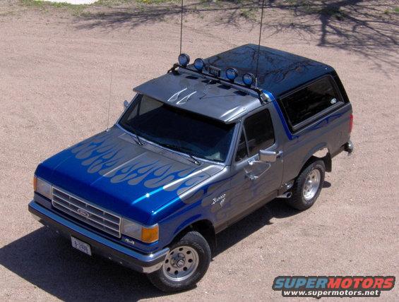 Blue and gray Ford Bronco with flame decals and light bar on top. License plate reads 8-2498