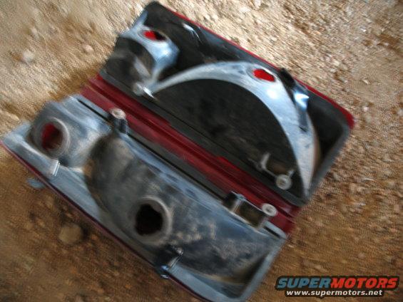 Two red car taillight assemblies, one disassembled, lying on dirt
