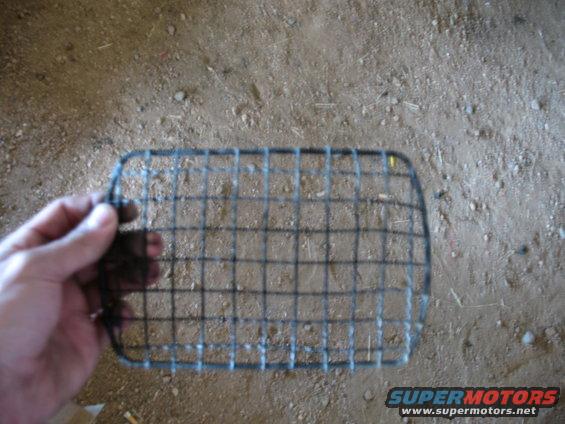 Hand holding a wire mesh grille, possibly for a vehicle headlight or radiator