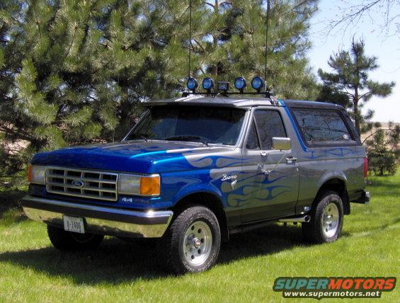 1987 Ford Bronco with blue and silver flame graphics, roof lights, and custom wheels