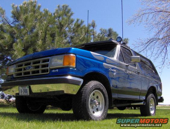 1987 Ford Bronco, blue with silver flame decals, parked on grass under a clear sky