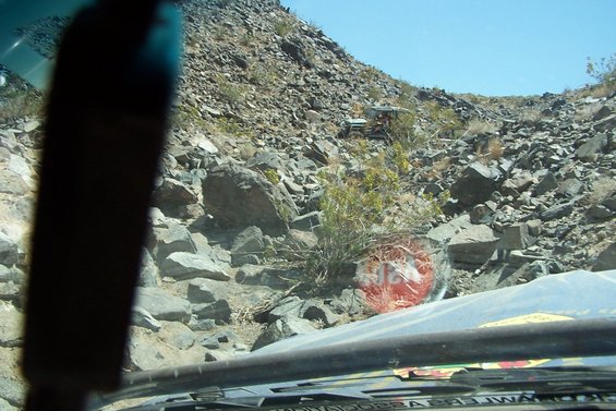 View from inside a vehicle looking out at a rocky, off-road landscape with two other vehicles visible in the distance