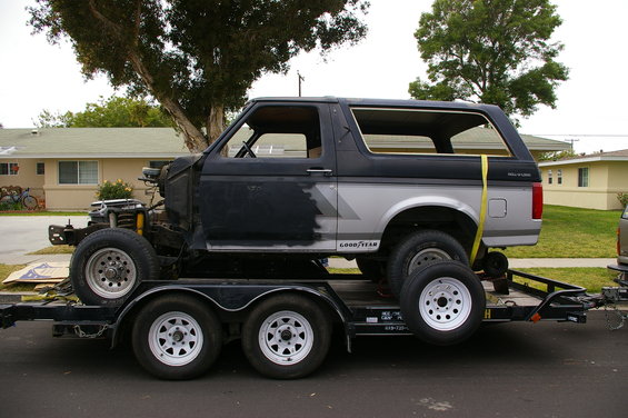 Black and silver Ford Bronco on a trailer, missing front end, side view