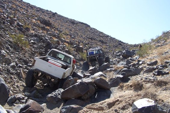 White pickup truck and rock crawler navigating a steep, rocky trail