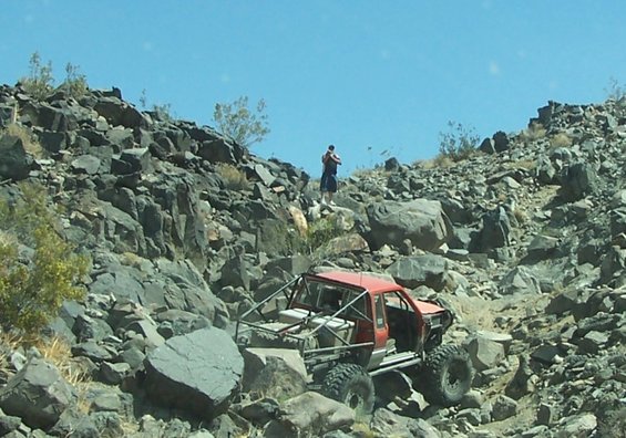 Red off-road vehicle with roll cage navigating rocky terrain