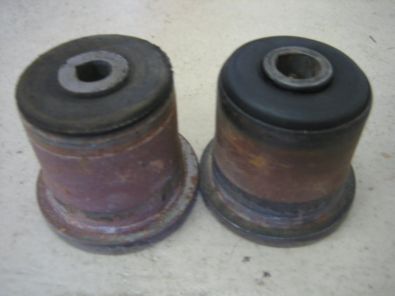 Two used suspension bushings, one with a black rubber top and the other with a worn metal top