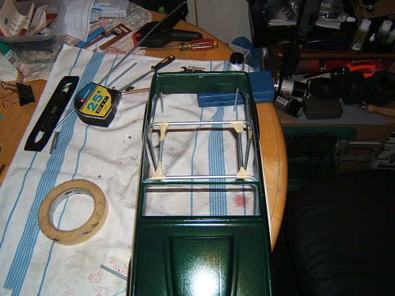 Green model car chassis with metal roll cage and beige plastic supports on a striped cloth