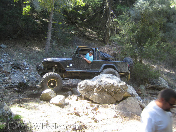 Black off-road vehicle with large tires navigating a rocky trail, driver visible