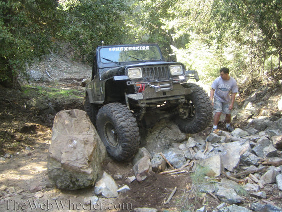 Black Jeep Wrangler with large tires navigating rocky terrain