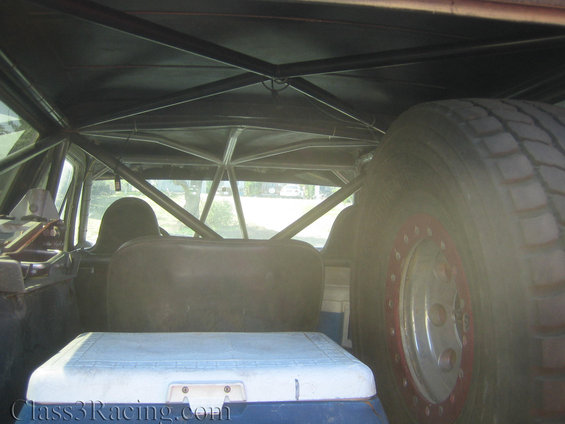 Interior of a vehicle with a roll cage, spare tire, and cooler. Red rim on spare tire