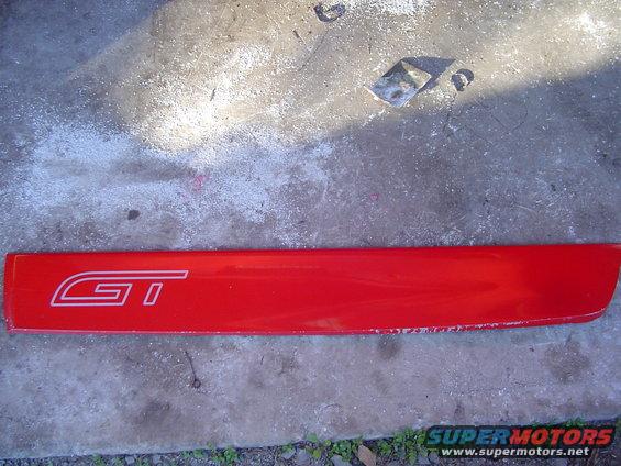 Red door trim piece with white GT emblem, showing wear and tear