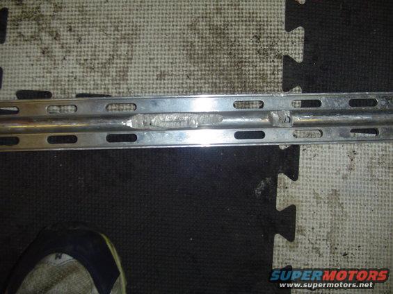 Metal bracket with welded repair and slotted holes, on a black and white puzzle mat