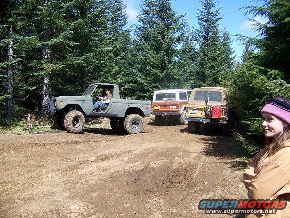 Three off-road vehicles on a dirt path in a forest, with a woman in the foreground