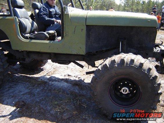 Green off-road vehicle with large tires, driver visible, side view