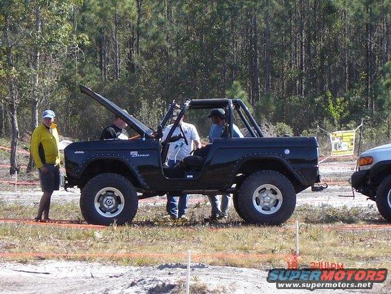 Black 1989 Ford Bronco side view with open hood and roll cage