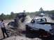 1989 Ford Bronco - Two off-road vehicles churn up dirt and dust during a competition with spectators gathered around.