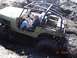 1989 Ford Bronco - An olive green off-road vehicle with a roll cage is stuck deep in mud, with two people inside.