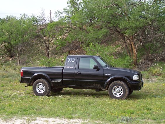 Black Ford Ranger pickup truck with "EDGE" on the side and "373 HEPLIN" on the door, parked in a grassy field