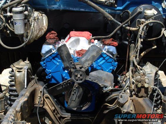 Engine bay with a blue V8 engine, fan, and various hoses and components. Some red cloths are placed on top of the engine